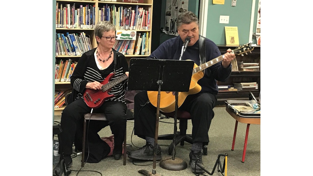 Two musicians performing with guitars inside the library